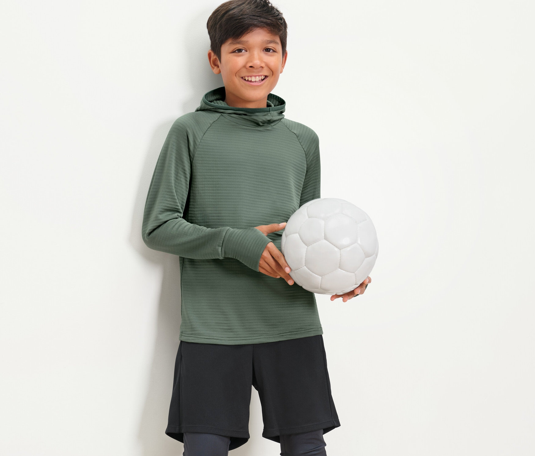 Ein Junge hält einen Fußball und trägt ein Kinder-Langarm-Funktionsshirt.