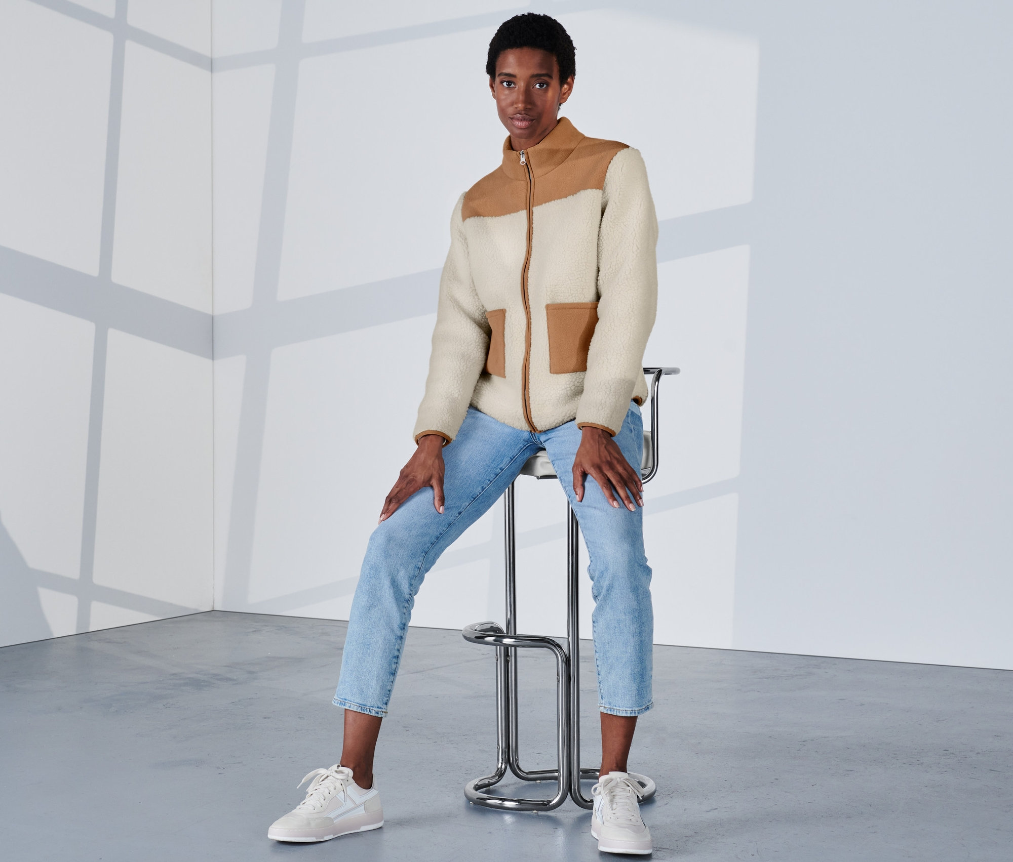 Frau sitzt auf einem Hocker und trägt eine Teddy-Jacke.