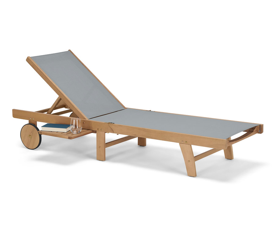 Graue Liege »Lenja« mit ausziehbarem Tabletttisch, auf dem ein Buch und ein Glas liegen.