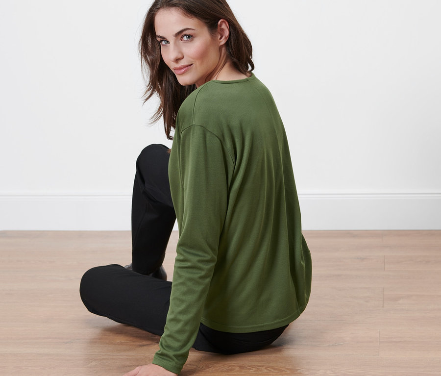 Frau sitzt auf dem Boden und trägt ein Blusenshirt.