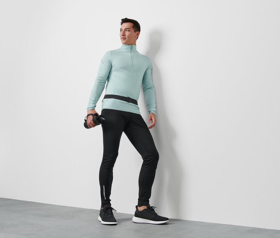 Mann trägt ein mintfarbenes Thermo-Funktionsshirt, eine Windprotection-Lauftight und einen Laufgürtel für Smartphones und hält eine Wasserflasche in der Hand.