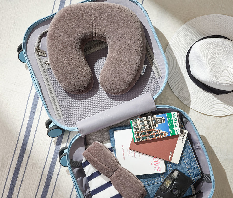 Im Koffer liegen ein graues TEMPUR® Transitkissen, eine Schlafmaske, ein Amsterdam-Reiseführer und eine Kamera.