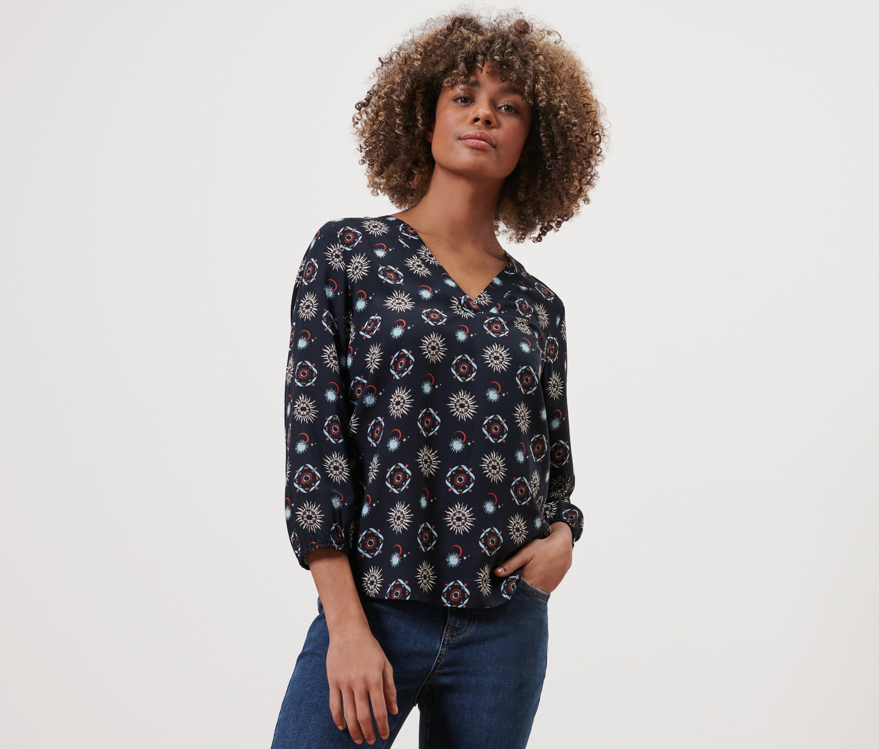 Frau posiert in einer Bluse mit Print und Jeans.