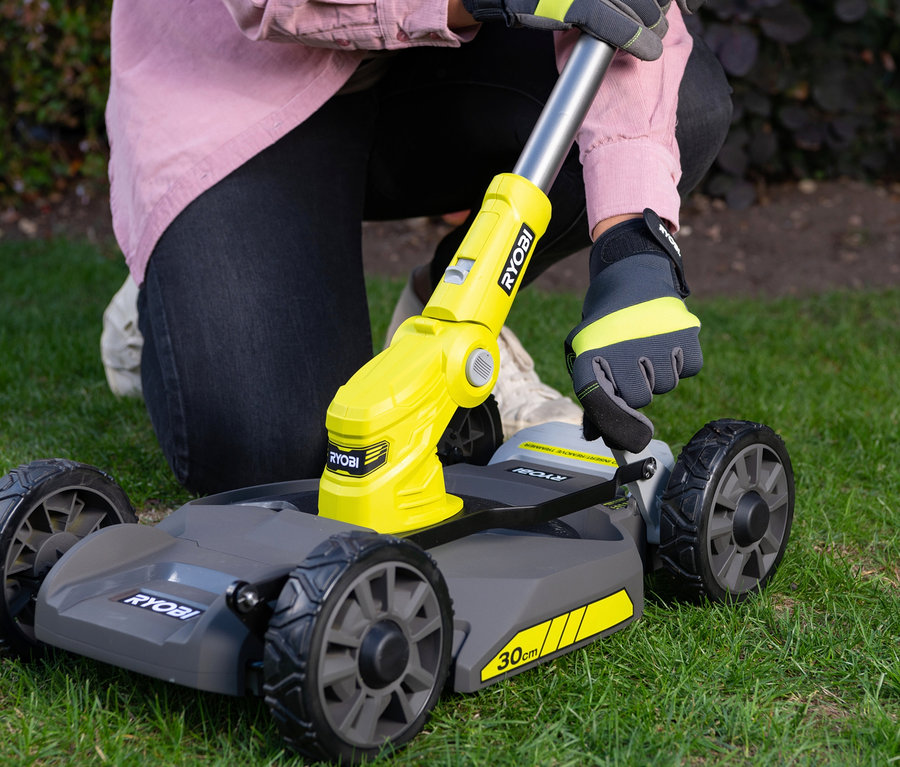 Frau kniet auf Gras und justiert RYOBI 18 V One+ Akku-City-Rasenmäher-Set »RY18LMC30A-120«.