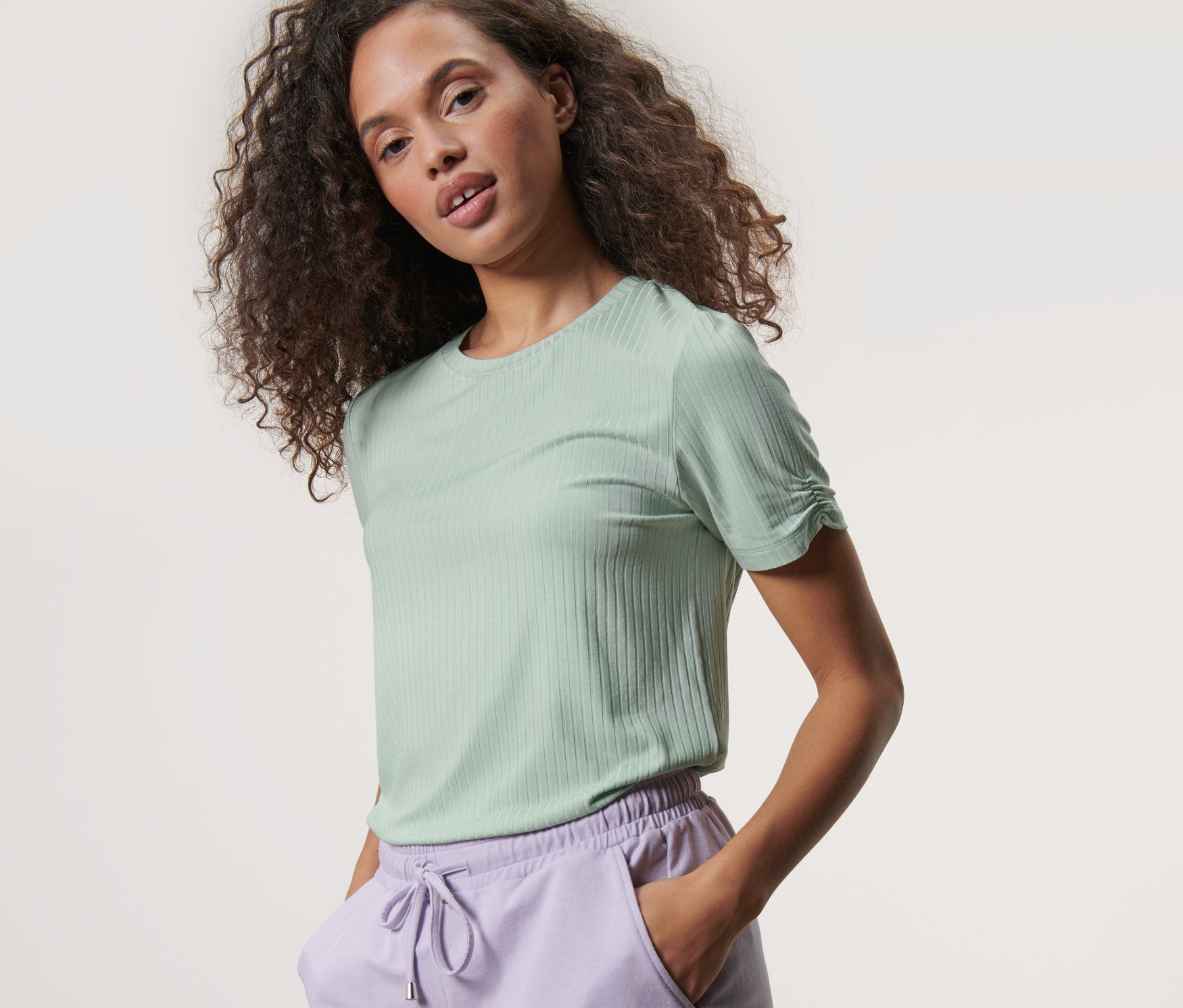 Frau trägt ein mintgrünes, geripptes Shirt und lila Shorts.
