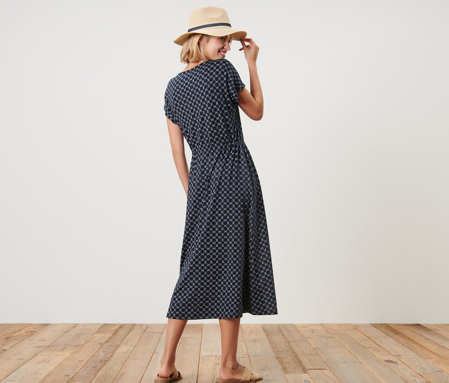 Frau lächelt über die Schulter und posiert in bedrucktem Jerseykleid und Hut.