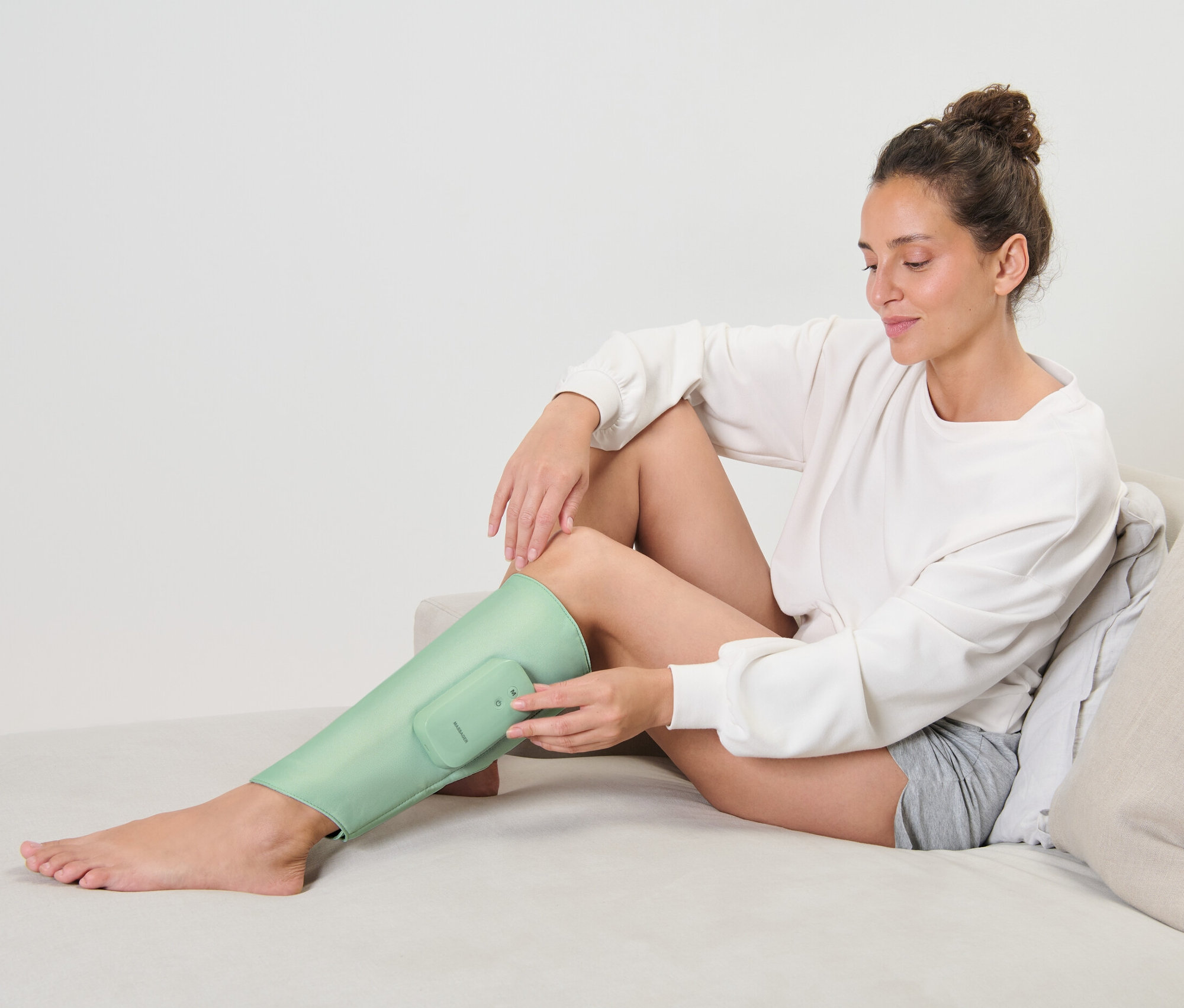 Frau sitzt auf Couch und nutzt Akku-Massage-Manschette am Bein.