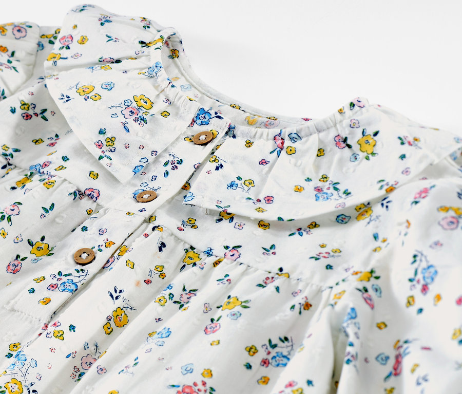 Detail einer Kinder-Bluse mit Blumenmuster und Zierkragen.