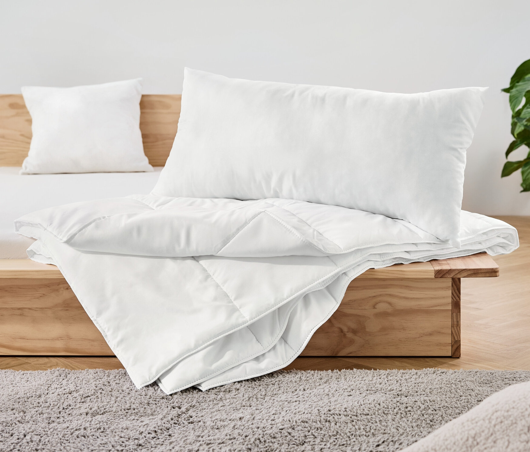 Auf einem Holzbett liegt ein weißes, 2-teiliges Betten-Set.