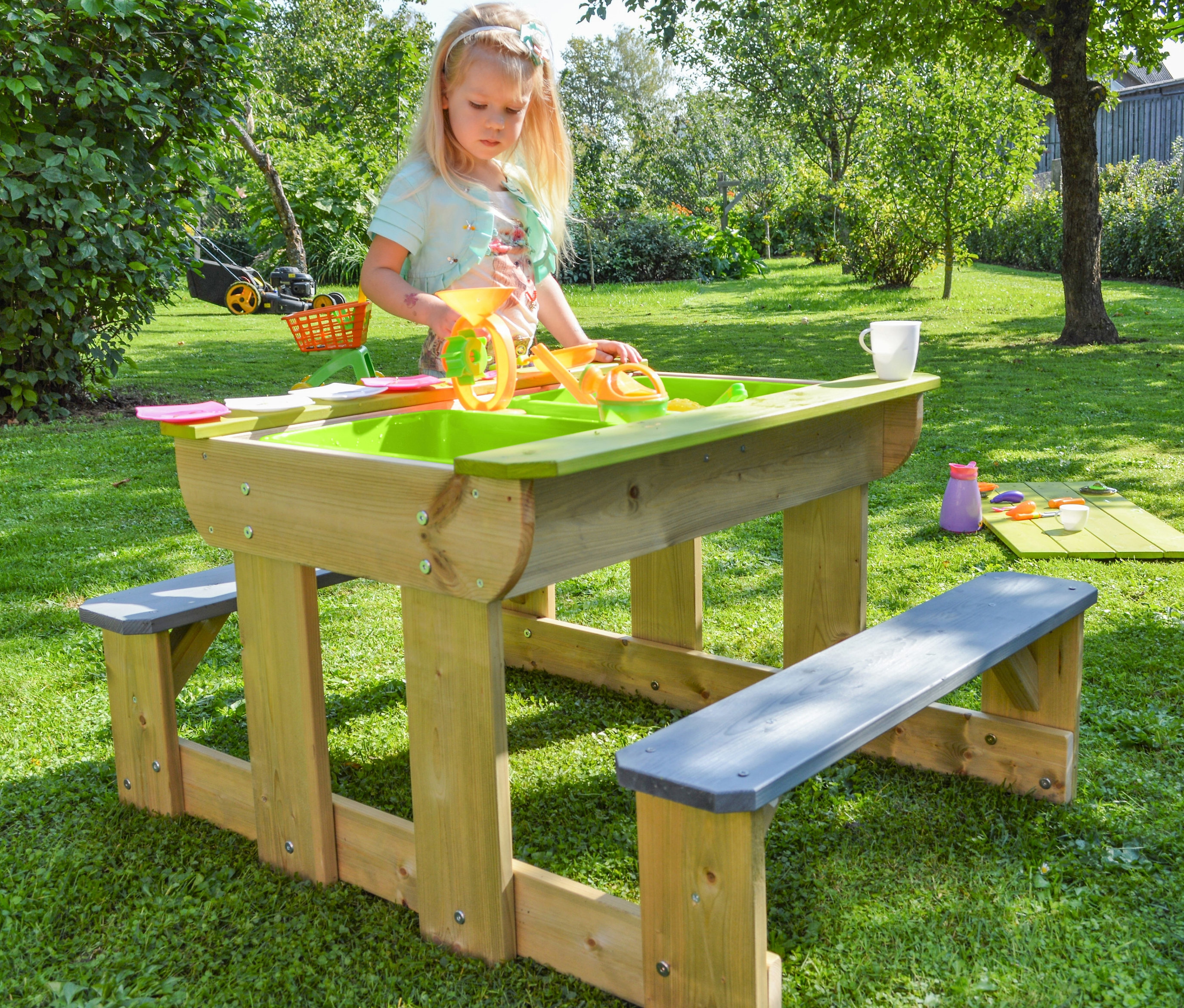Mädchen spielt am Wendi Picknick- und Matschtisch mit Bänken auf einer Wiese.