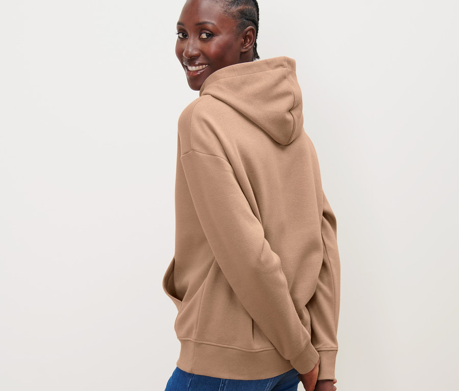 Frau blickt über die Schulter und posiert in einem beigen Hoodie.