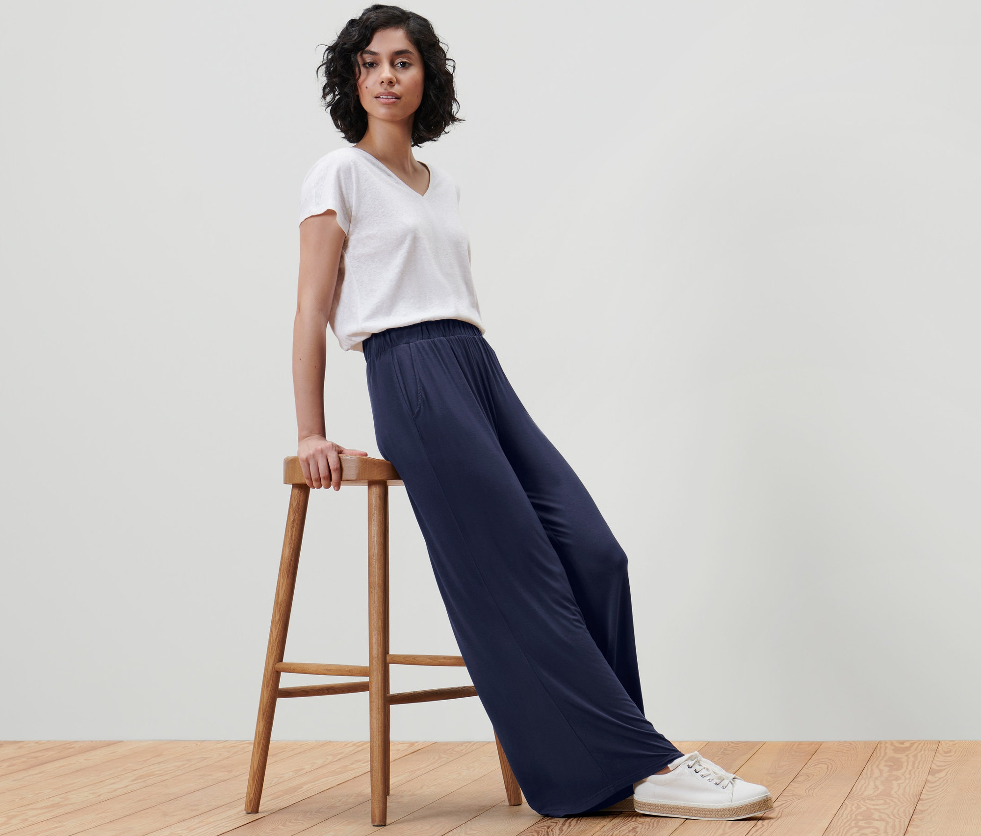 Frau sitzt auf einem Hocker und trägt eine dunkelblaue Palazzohose.