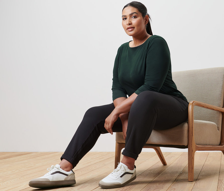 Frau sitzt im Sessel und trägt ein Shirt mit 3/4-Arm, eine Joggpants und Leder-Sneaker.