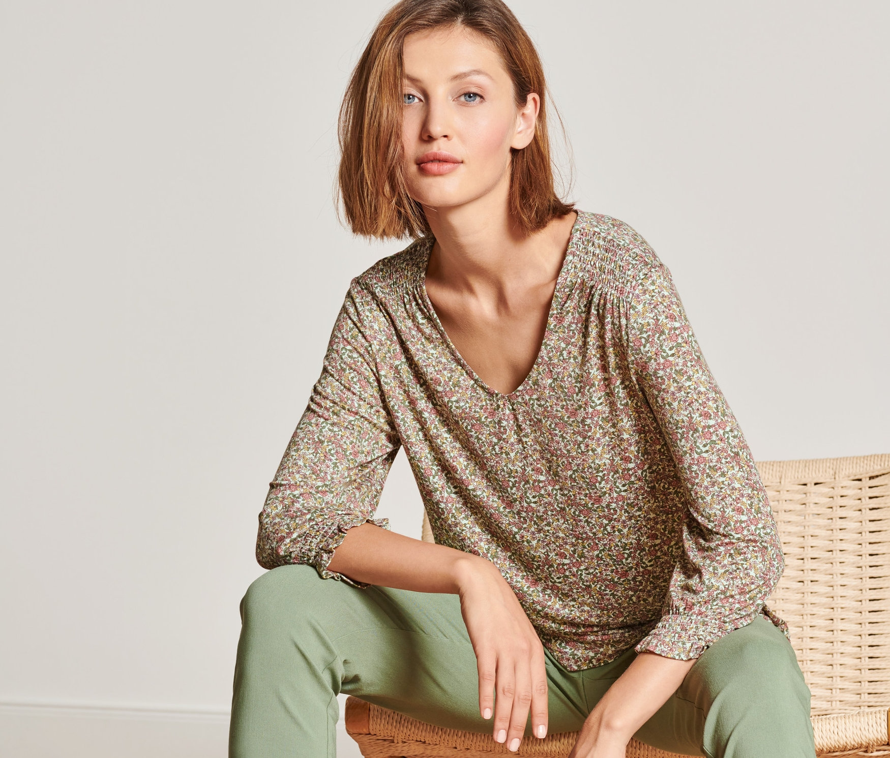 Frau sitzt auf einem Stuhl und trägt ein Blusenshirt mit 3/4-Arm.