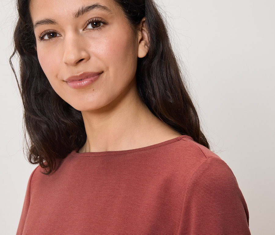 Porträt einer lächelnden Frau mit braunen Haaren in einer braunen Bluse.