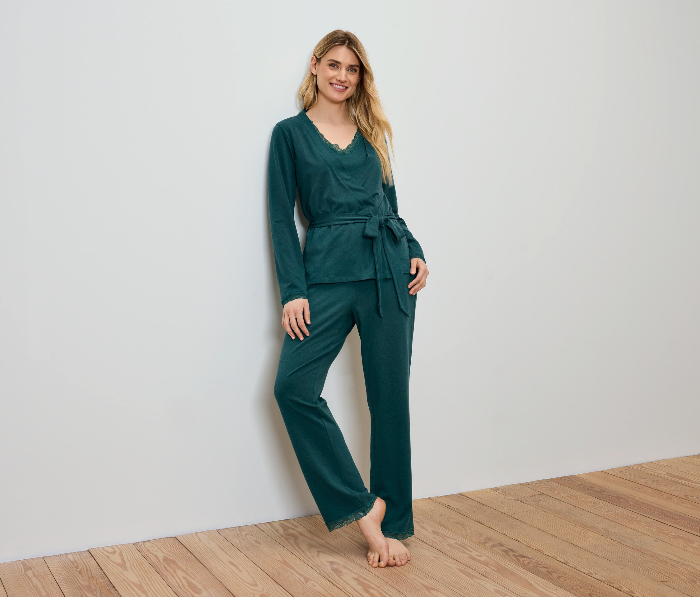 Frau im grünen Pyjama steht an einer Wand.