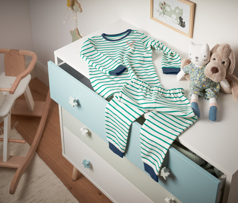 Gestreifter Interlock-Pyjama aus Bio-Baumwolle liegt auf einer Kommode neben Stofftieren.