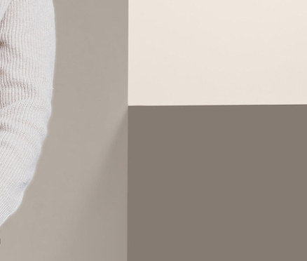 Lächelndes Mädchen an eine Wand gelehnt trägt eine Stretchhose und einen Strickpullover.