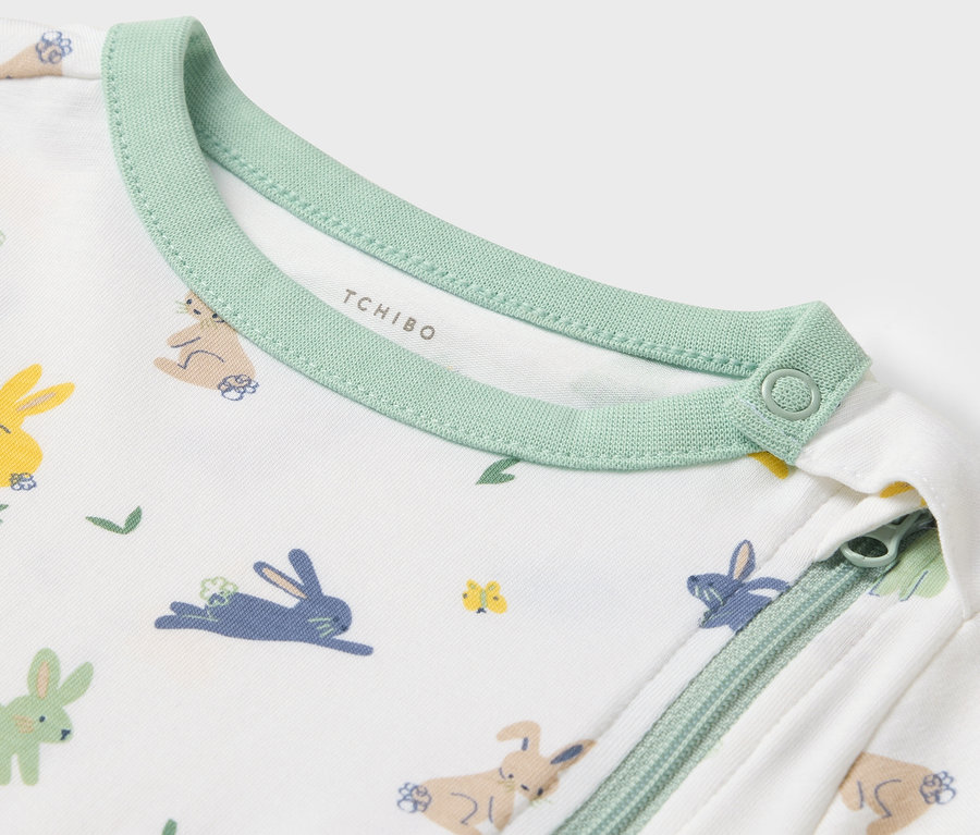 Detailaufnahme eines Baby-Overalls mit Hasenmuster und grünem Rand.