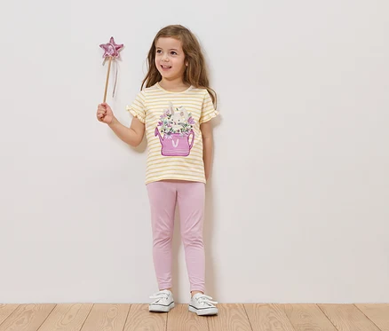 Mädchen hält einen Sternenstab und trägt ein gestreiftes T-Shirt mit einer Gießkanne und Blumen darauf, sowie eine rosafarbene Leggings.