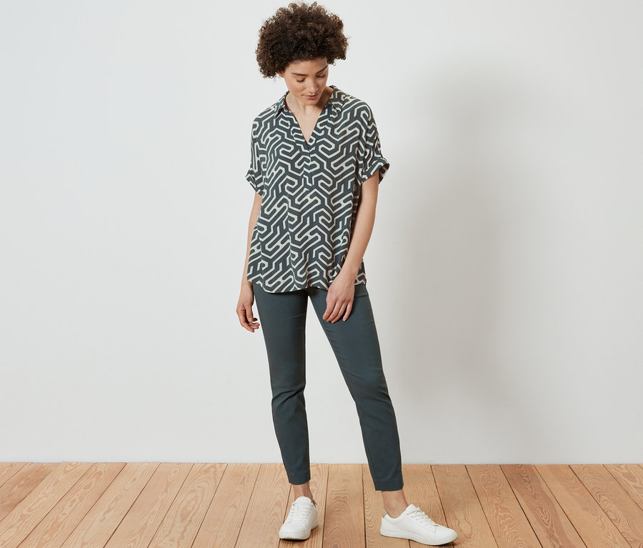 Frau steht und trägt eine bedruckte Bluse.