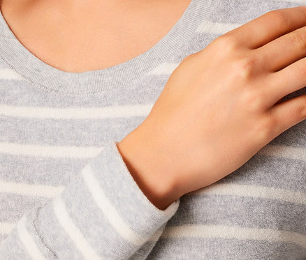 Detailaufnahme eines grauen Damenpullovers mit weißen Streifen und einer Hand auf der Brust.