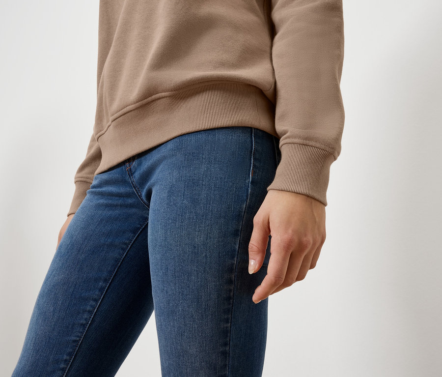 Nahaufnahme einer Frau mit beigem Pullover und blauen Jeans.