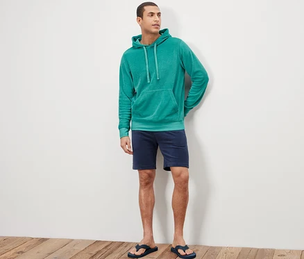 Mann steht und trägt einen Frottee-Hoodie, Shorts und Flip-Flops.