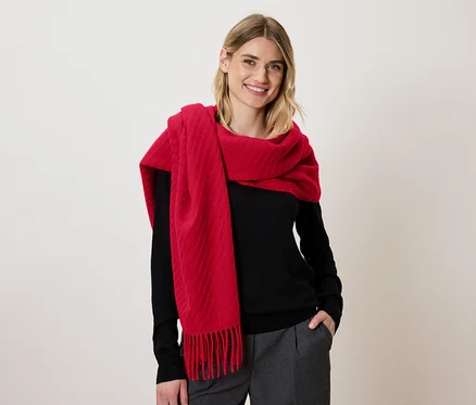 Eine blondhaarige Frau lächelt und trägt einen roten Schal und einen schwarzen Pullover.