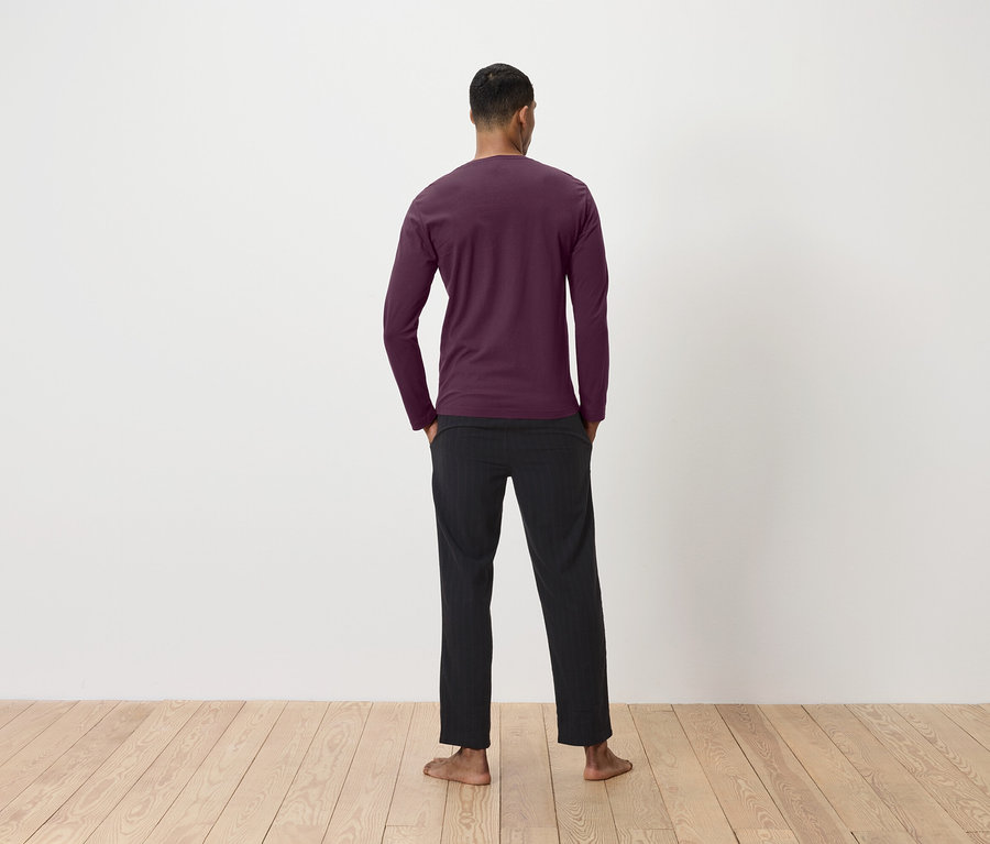 Mann von hinten trägt ein weinrotes Langarmshirt und eine schwarze Hose.