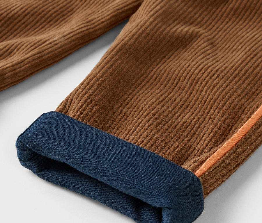 Detail einer braunen Cordhose mit dunkelblauem Saum am Hosenbein.