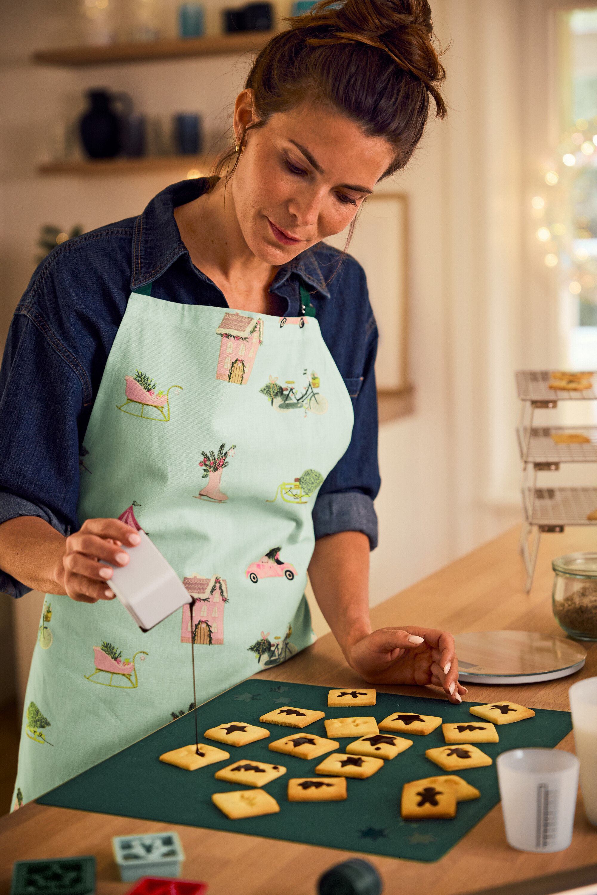 Frau mit Schürze verziert Kekse mit Zuckerguss auf einer grünen Matte.