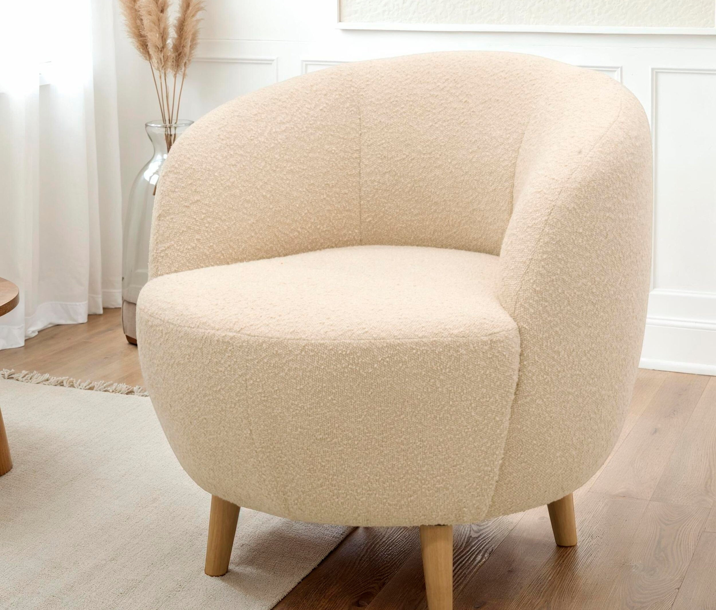 Cremefarbener Sessel mit Holzbeinen auf einem Teppich.