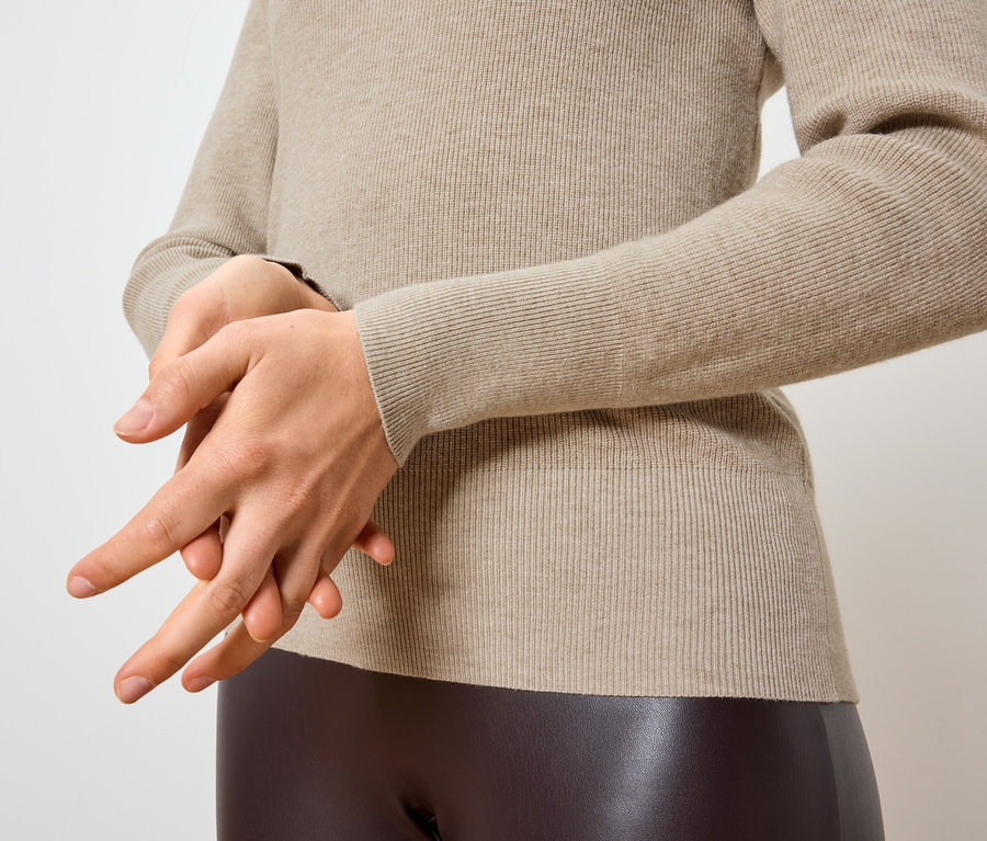 Frau reibt sich die Hände vor einem cremefarbenen Pullover und braunen Leggings.
