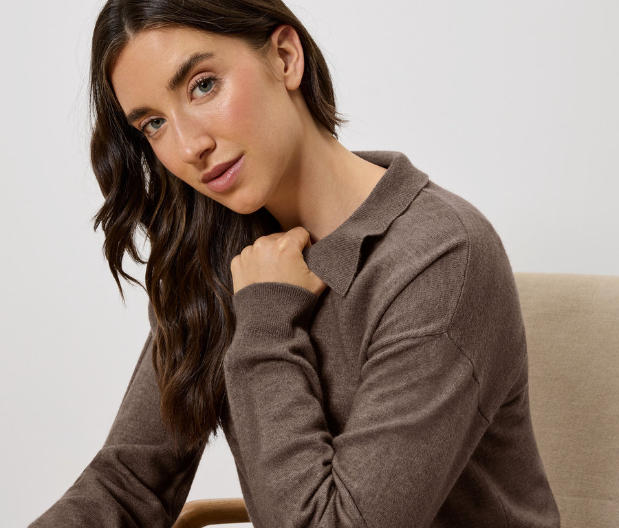 Eine Frau sitzt auf einem Stuhl und trägt einen braunen Pullover mit Kragen.