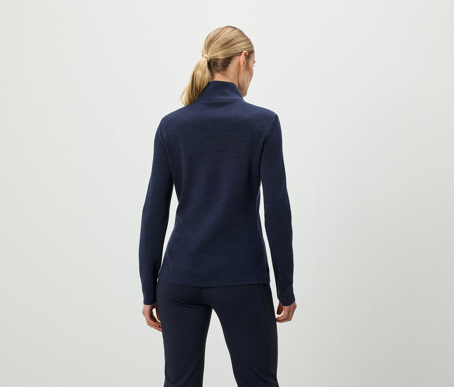 Von hinten ist eine Frau mit blonden, zu einem Pferdeschwanz zusammengebundenen Haaren zu sehen, die ein dunkelblaues Langarmshirt und eine dunkelblaue Hose trägt.