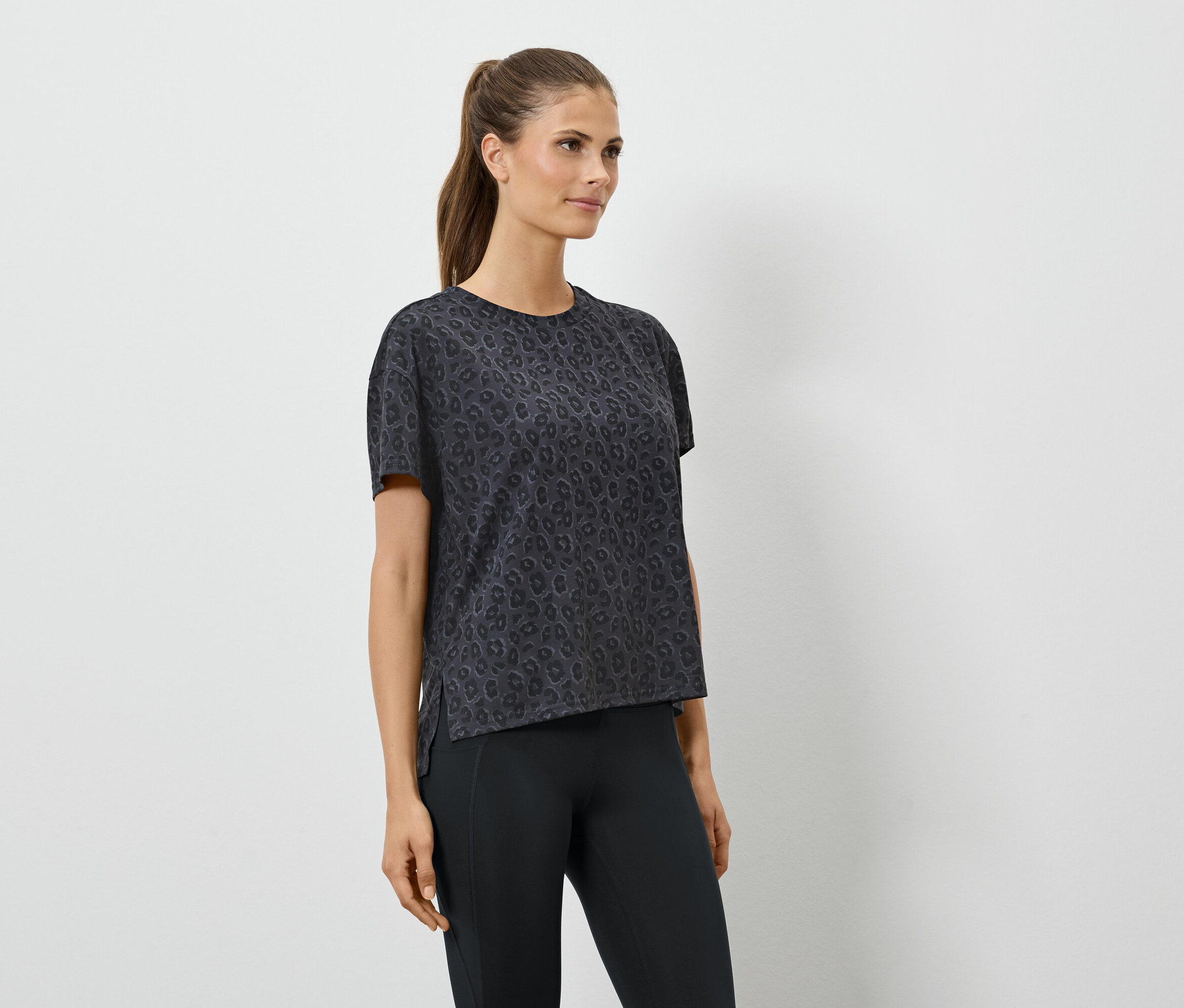 Frau in einem schwarzen Sport-T-Shirt mit kurzen Ärmeln und schwarzen Leggings.