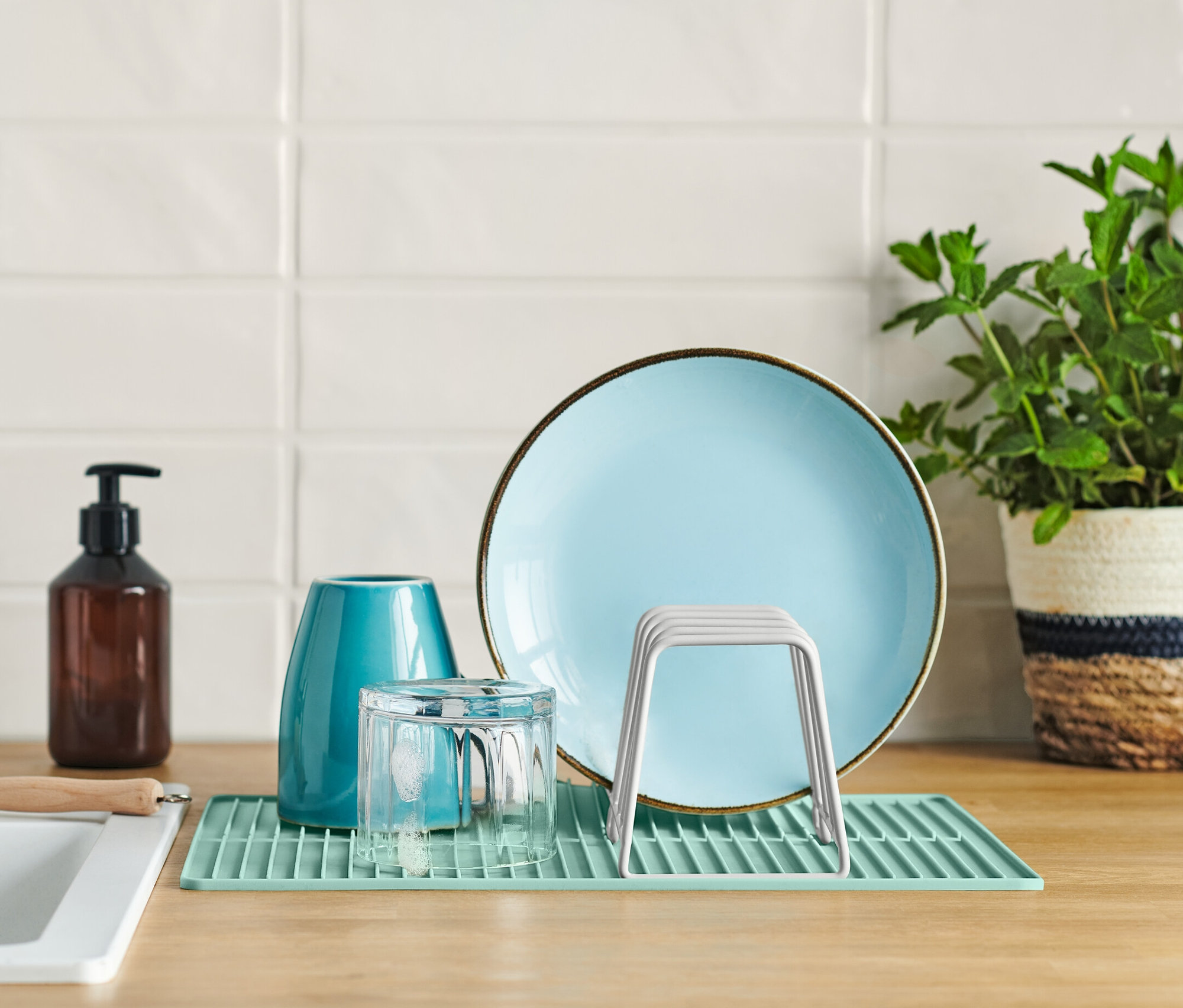 Blauer Teller, Glas und Abtropfgestell mit Silikonmatte auf einer Küchentheke neben einem Spülbecken.