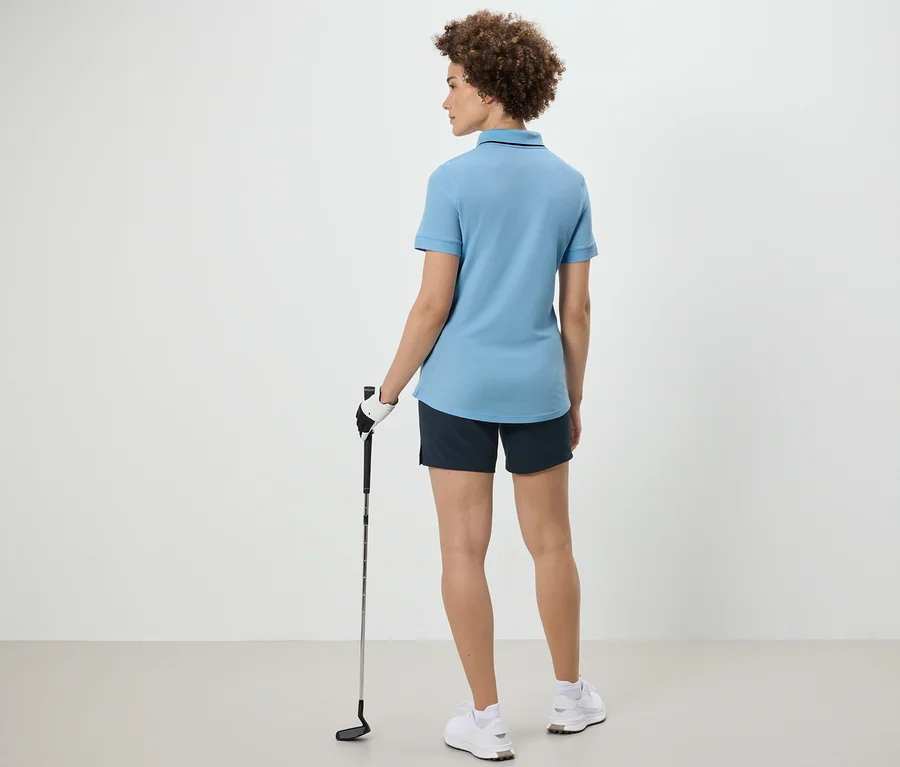 Frau von hinten hält einen Golfschläger und trägt ein hellblaues Funktionspoloshirt.
