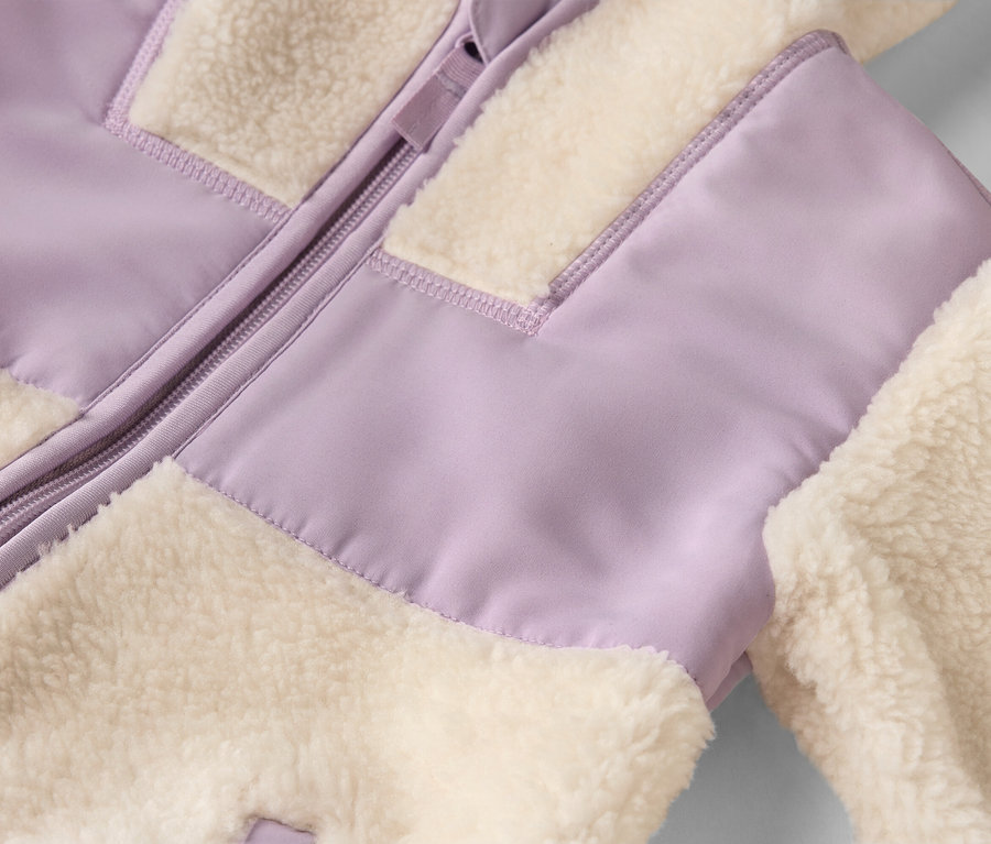Nahaufnahme einer Jacke mit Reißverschluss und flauschigen, cremefarbenen und lavendelfarbenen Stoffbahnen.