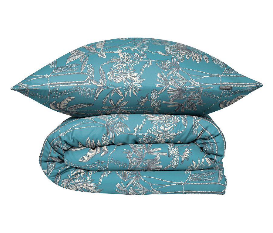 Ein blaues Kissen liegt auf einer gefalteten blauen Bettdecke mit weißem tropischen Pflanzenmuster.