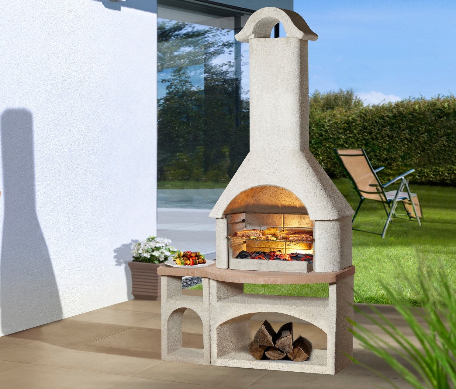 Buschbeck Gartengrillkamin »Bozen« steht auf einer Terrasse, Grillgut liegt auf dem Rost.