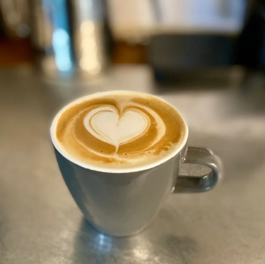 Nahaufnahme einer grauen Tasse mit einem Latte Macchiato, dessen Milchschaum ein Herz formt.