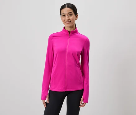Frau mit Pferdeschwanz trägt pinke Jacke mit Reißverschluss und schwarze Leggings vor grauem Hintergrund.