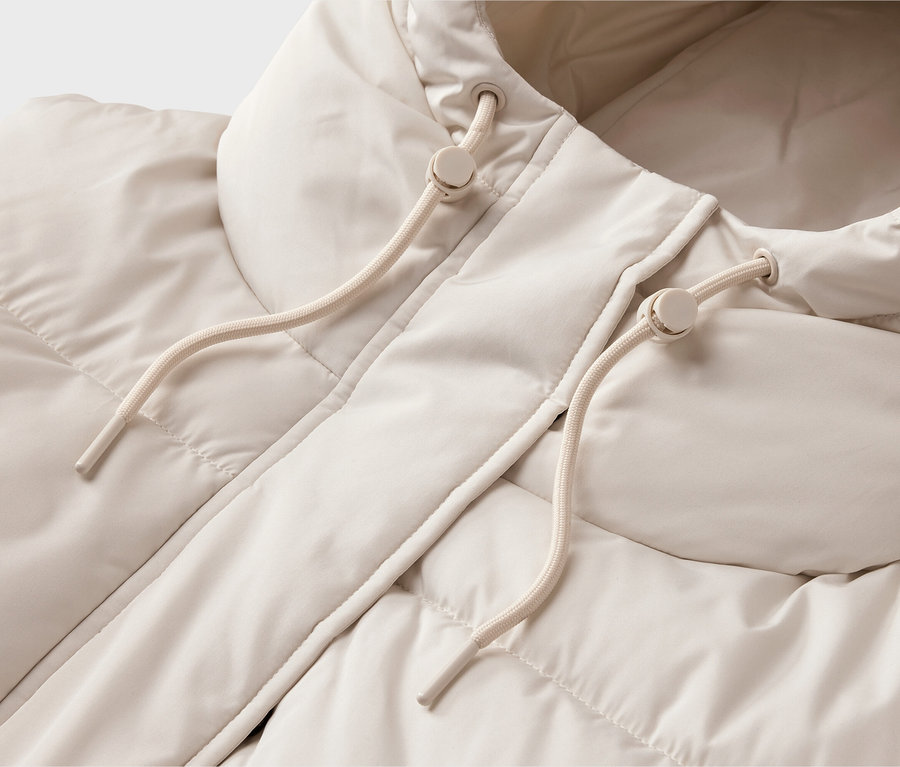 Nahaufnahme einer hellbeigen Steppjacke mit Kapuze. Die Jacke hat eine gesteppte Textur und die Kapuze ist mit zwei cremefarbenen Kordelzügen mit Kunststoffstoppern versehen.