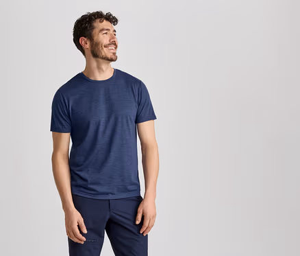 Ein Mann in einem blauen T-Shirt und einer dunkelblauen Hose lächelt und blickt nach rechts.