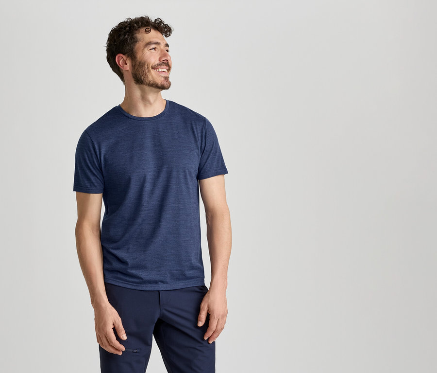 Ein Mann in einem blauen T-Shirt und einer dunkelblauen Hose lächelt und blickt nach rechts.