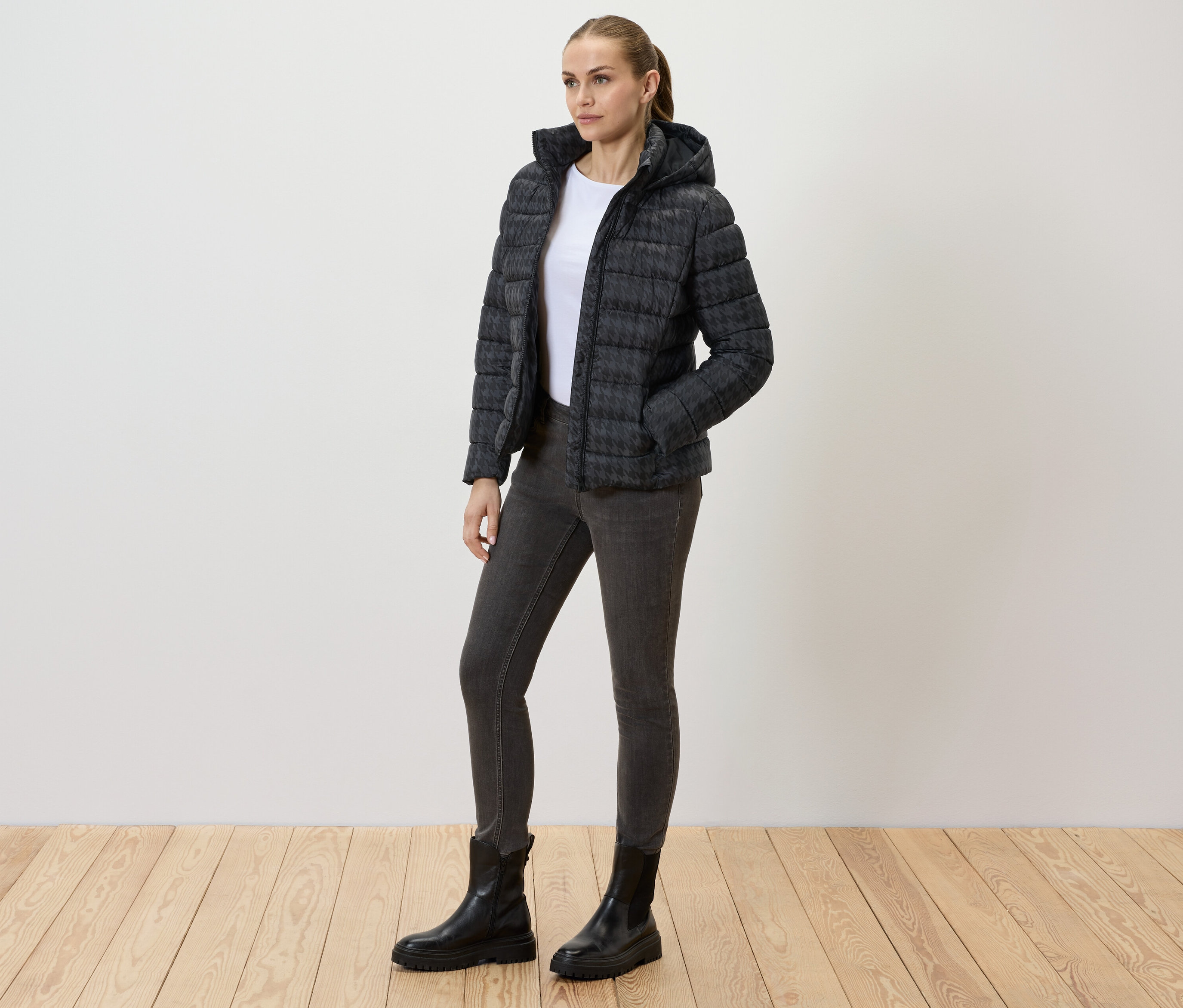 Frau trägt eine bedruckte Steppjacke mit Kapuze, Jeans und schwarze Stiefel.