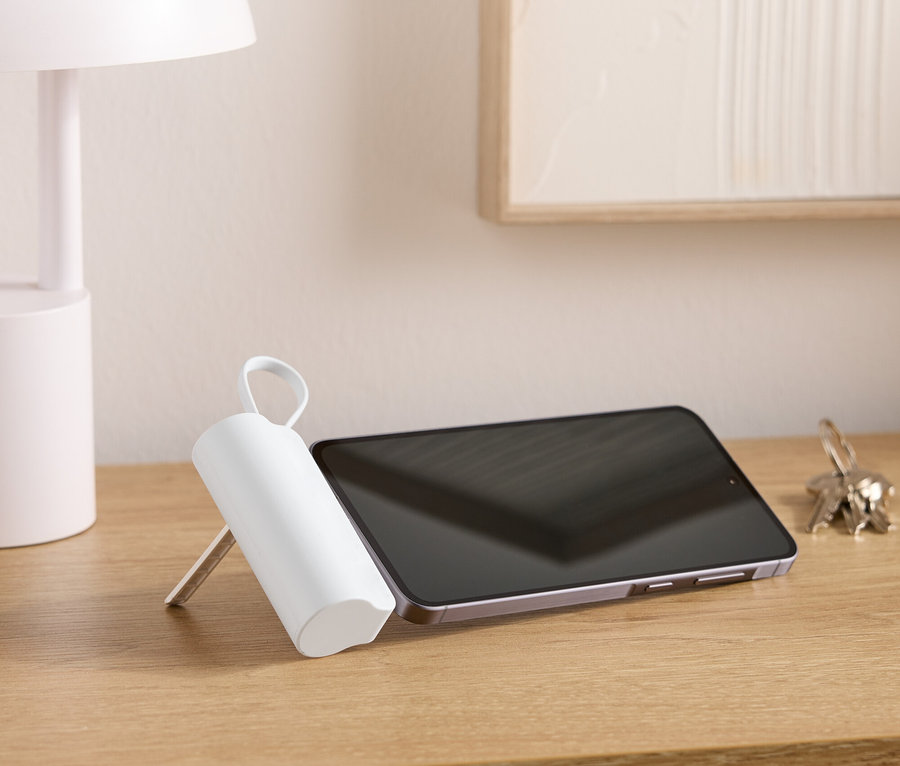 Auf einem Holztisch stehen eine Lampe, ein Tablet, ein Schlüsselbund und ein weisser, zylinderförmiger Gegenstand mit einem Griff.