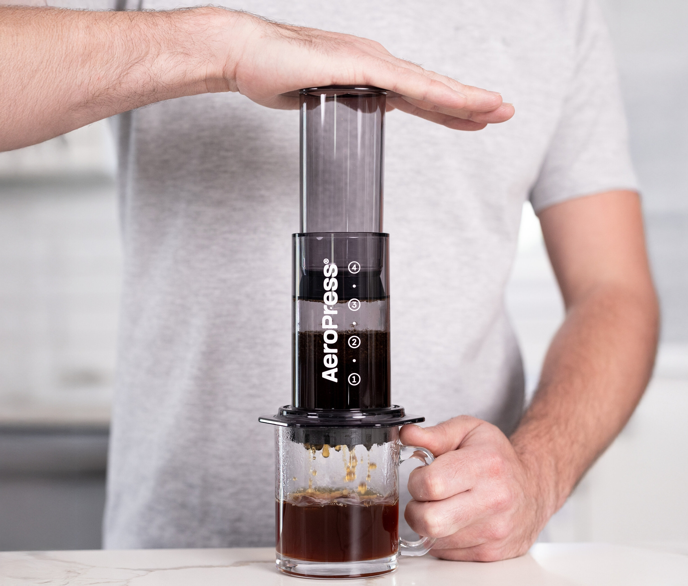 Eine Person drückt einen schwarzen AeroPress Coffee Maker »Clear« über einer Tasse herunter.